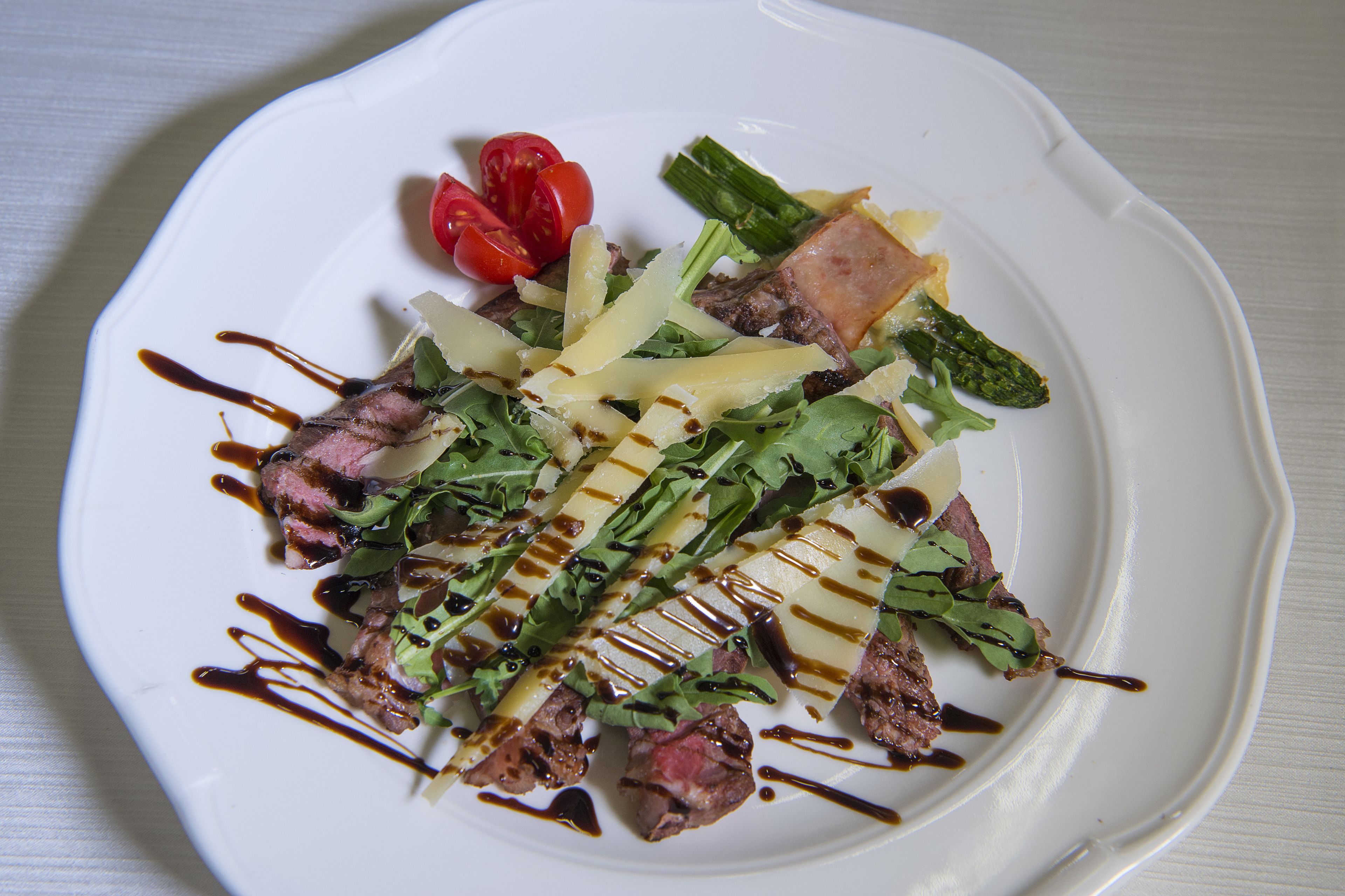 A white plate with a salad containing asparagus, tomatoes, and meat, drizzled with sauce.