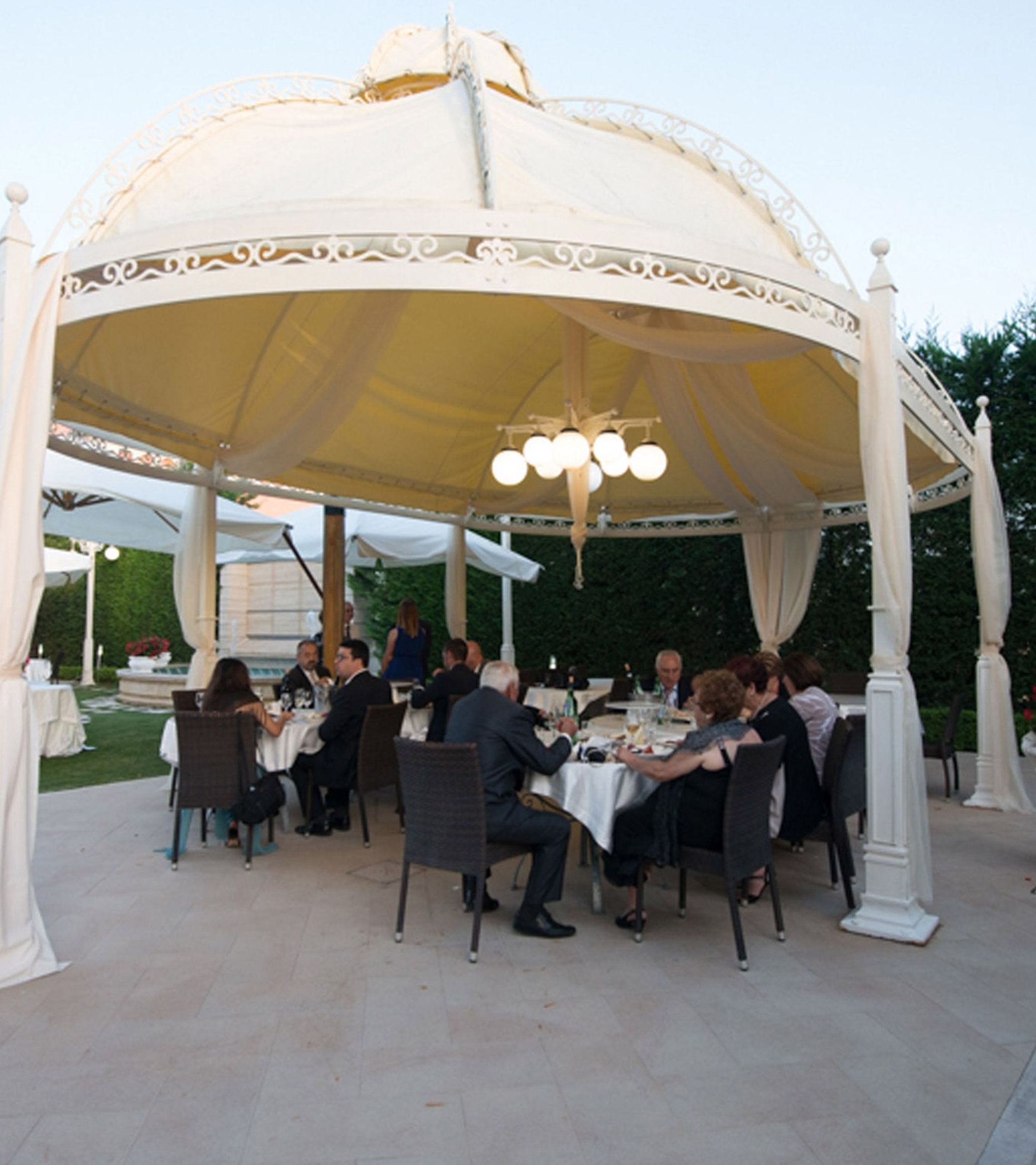 Ein Pavillon mit weißer Kuppel und Säulen, umgeben von Tischen und Stühlen zum Essen.