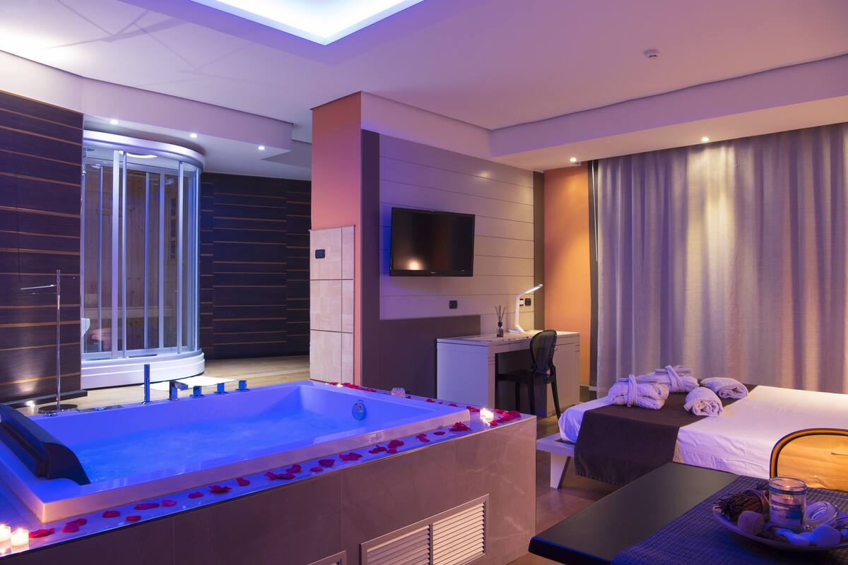 Ein modernes Hotelzimmer mit einer großen Badewanne, einem Schreibtisch, einem Bett und einem Fernseher.