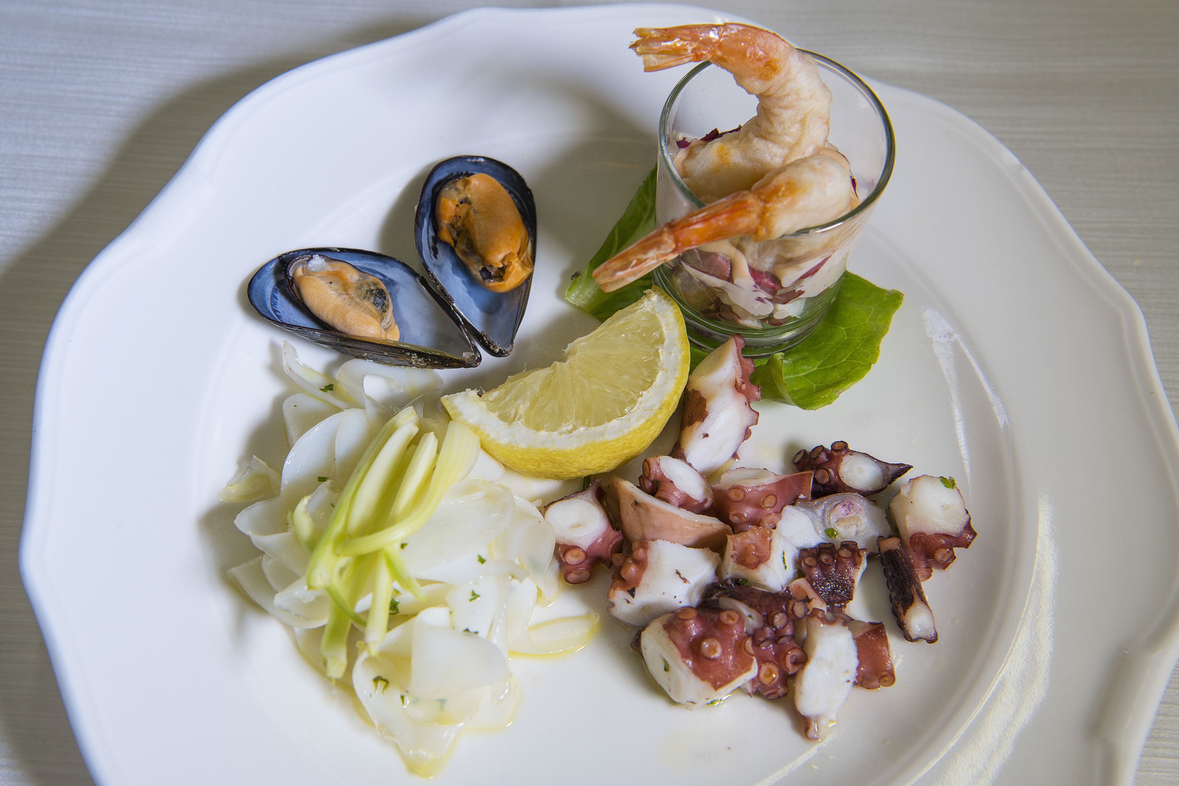 Un plato de mariscos con mejillones, camarones, pulpo y limón.