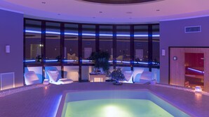 A spa area with a large hot tub, seating, and a view of the cityscape through large windows.