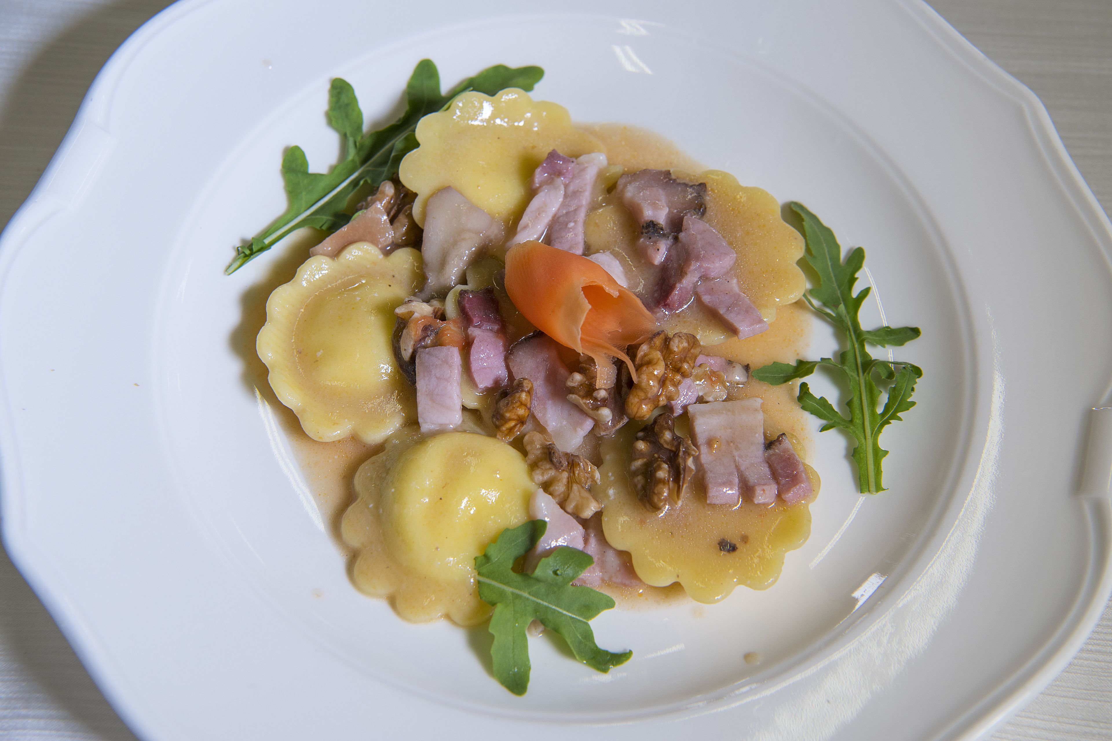 A plate of food with ravioli, ham, walnuts, and greens.