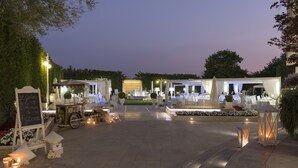 An outdoor event space with tables set for dining, surrounded by decorative elements and lighting.
