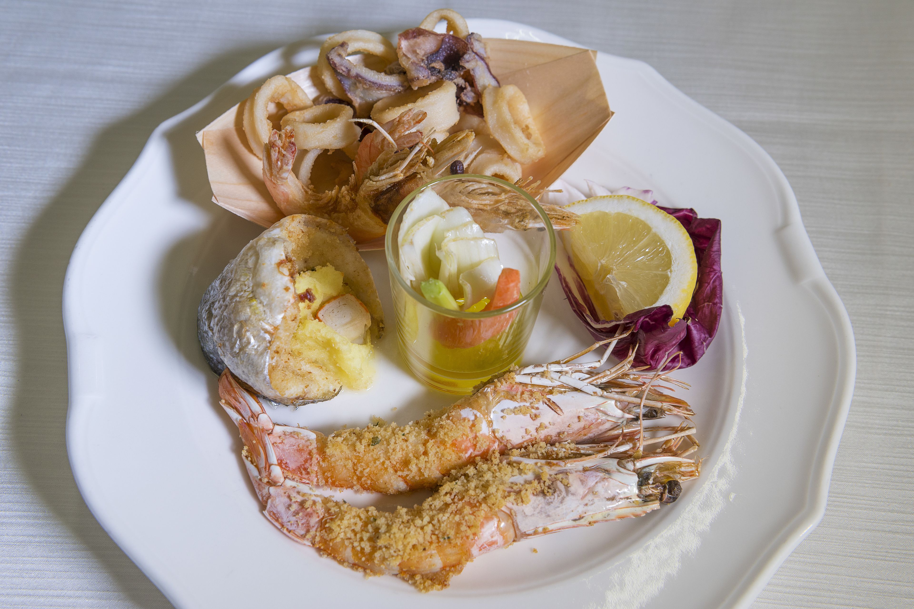Une assiette de fruits de mer comprenant des crevettes, des calamars et une tranche de citron.