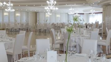 Une salle à manger formelle avec des tables, des chaises et des lustres élégants, le tout dans des tons blancs.