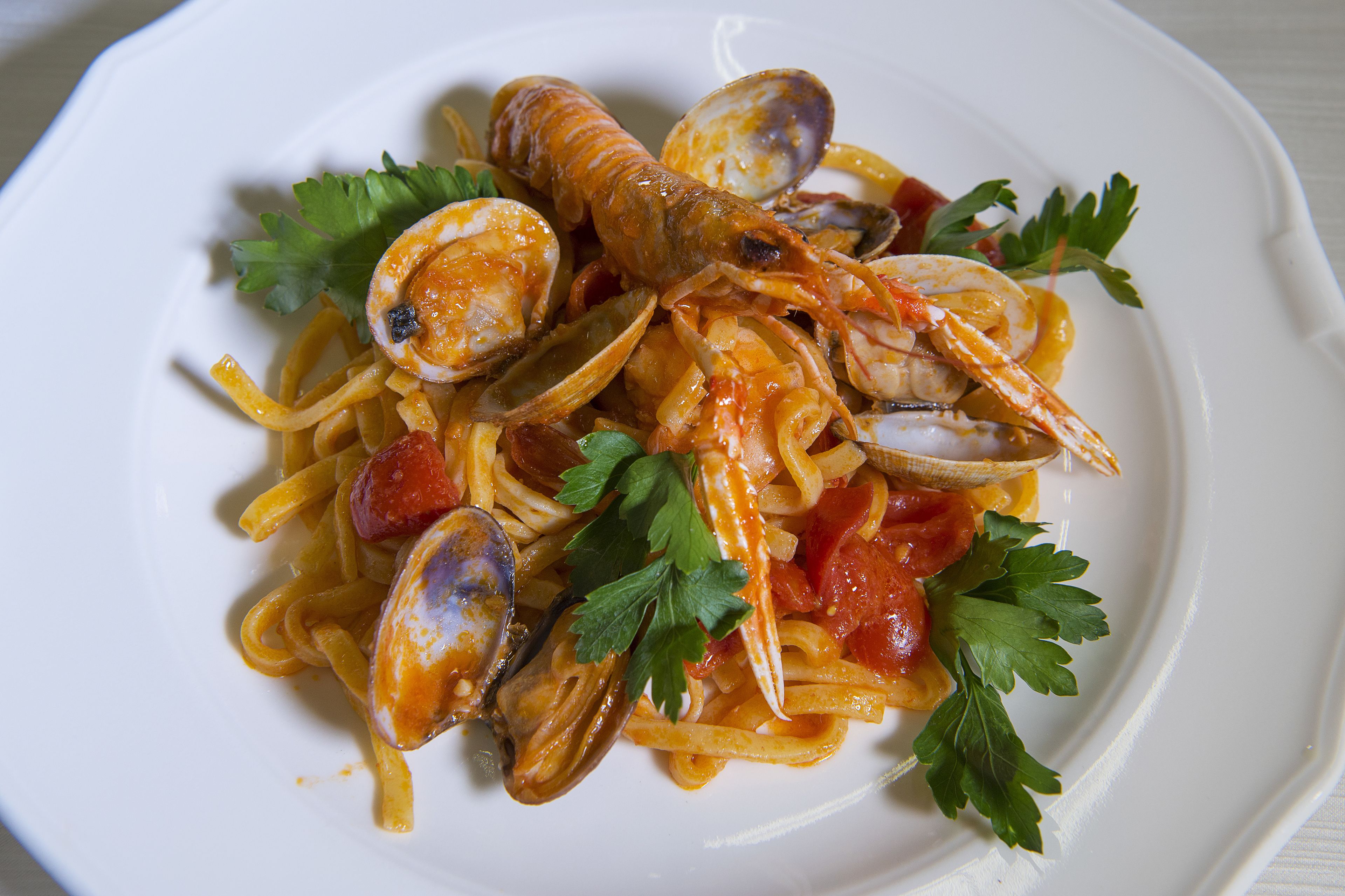 Un plato de pasta con almejas y tomates, adornado con perejil.