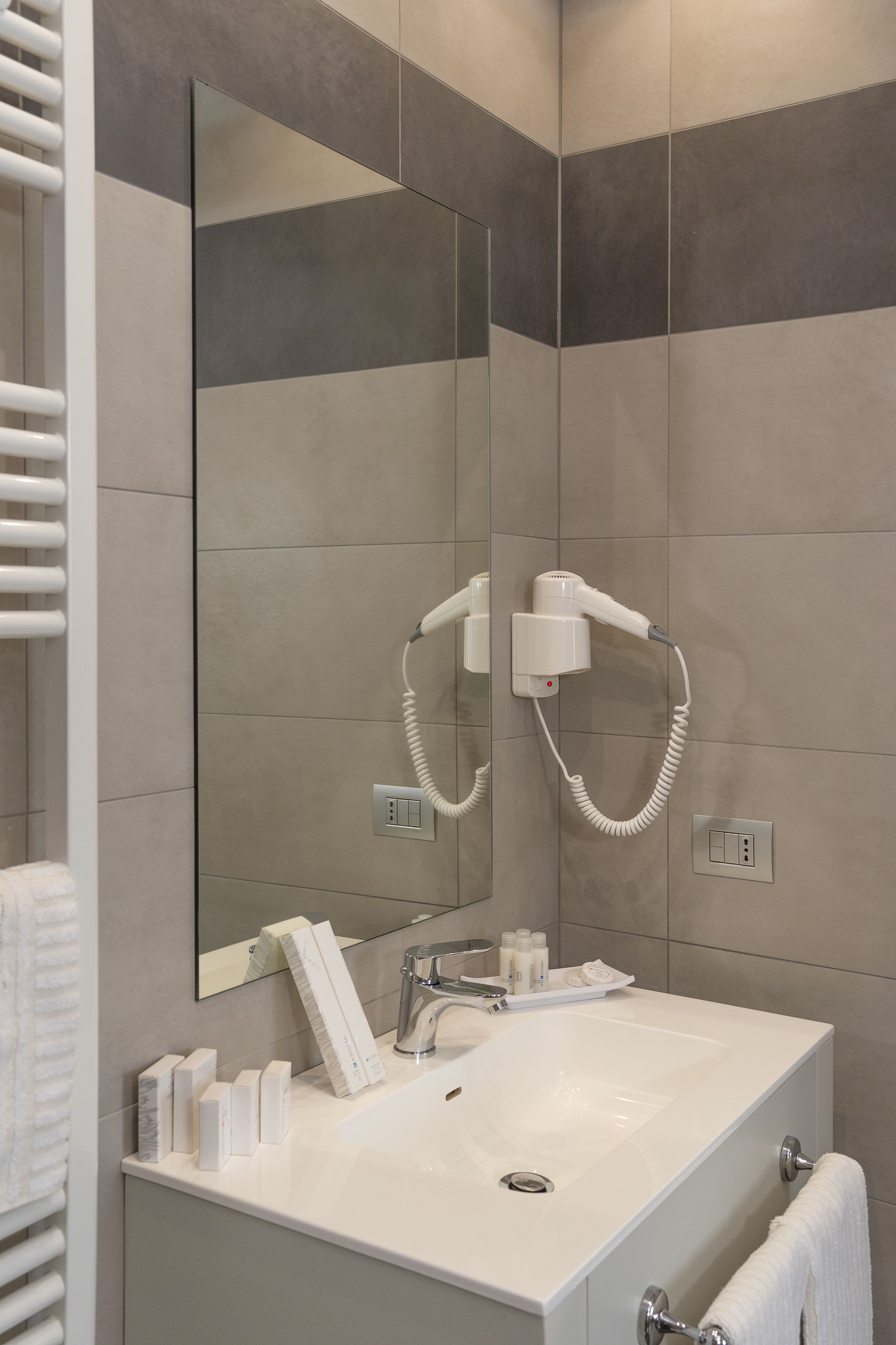 A modern bathroom with a large mirror, a hairdryer, a sink, and toiletries.