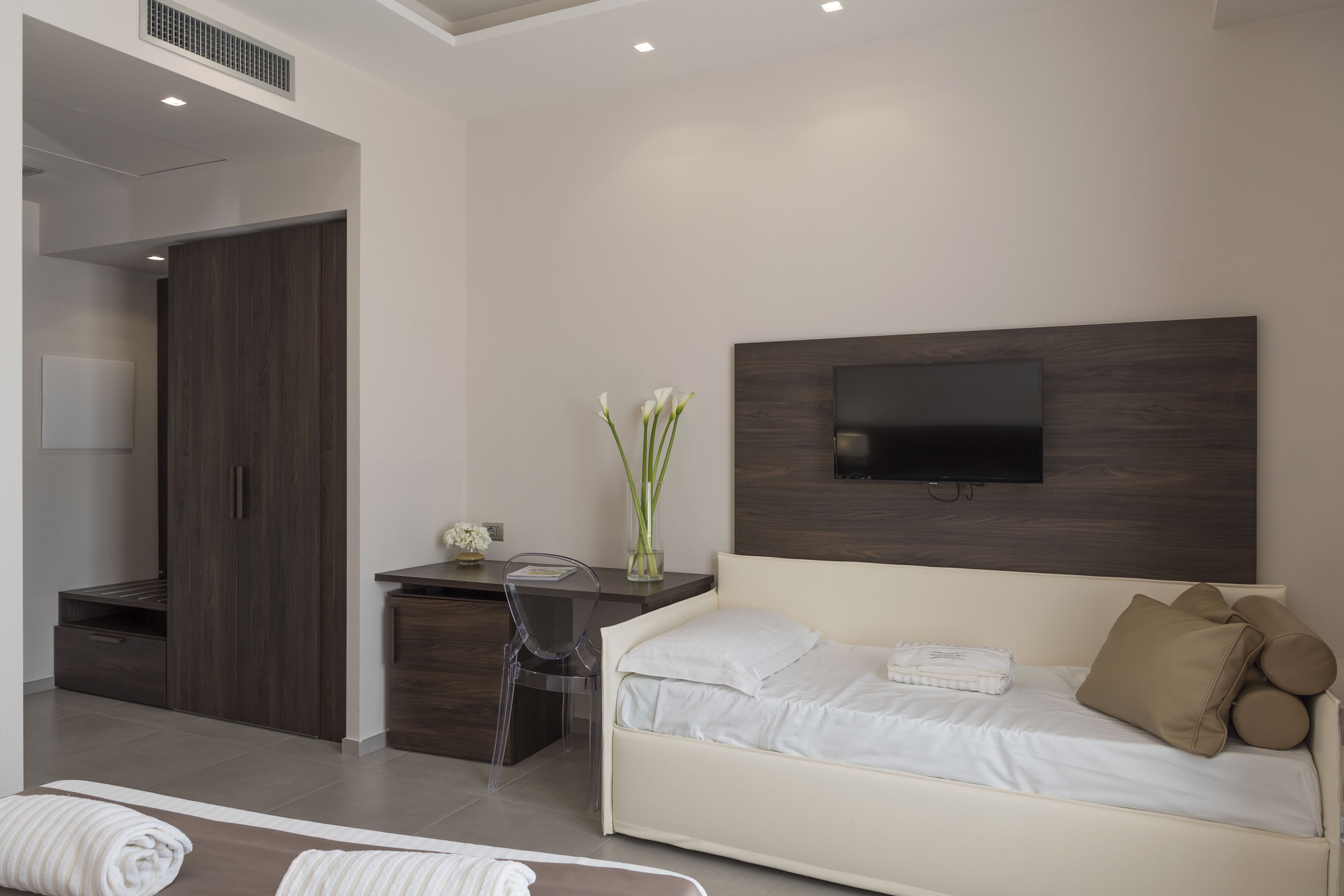A modern hotel room with a bed, a desk, a chair, and a TV mounted on the wall.