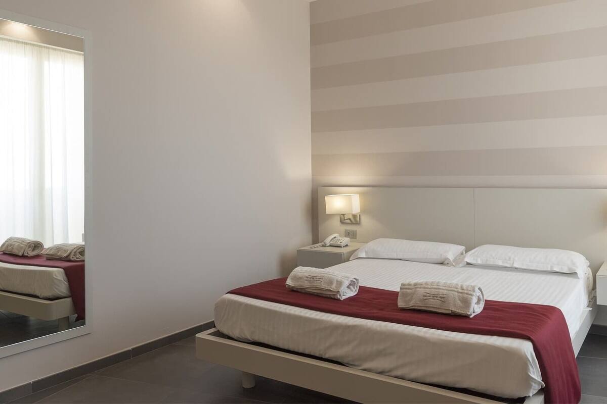 Ein Hotelzimmer mit einem großen Bett, zwei Nachttischen mit Lampen, einem Spiegel und Blick auf den Himmel.