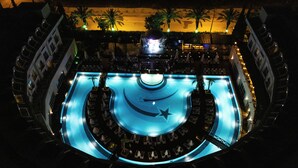 Una piscina interior con escenario central, rodeada de sillones de descanso y palmeras.