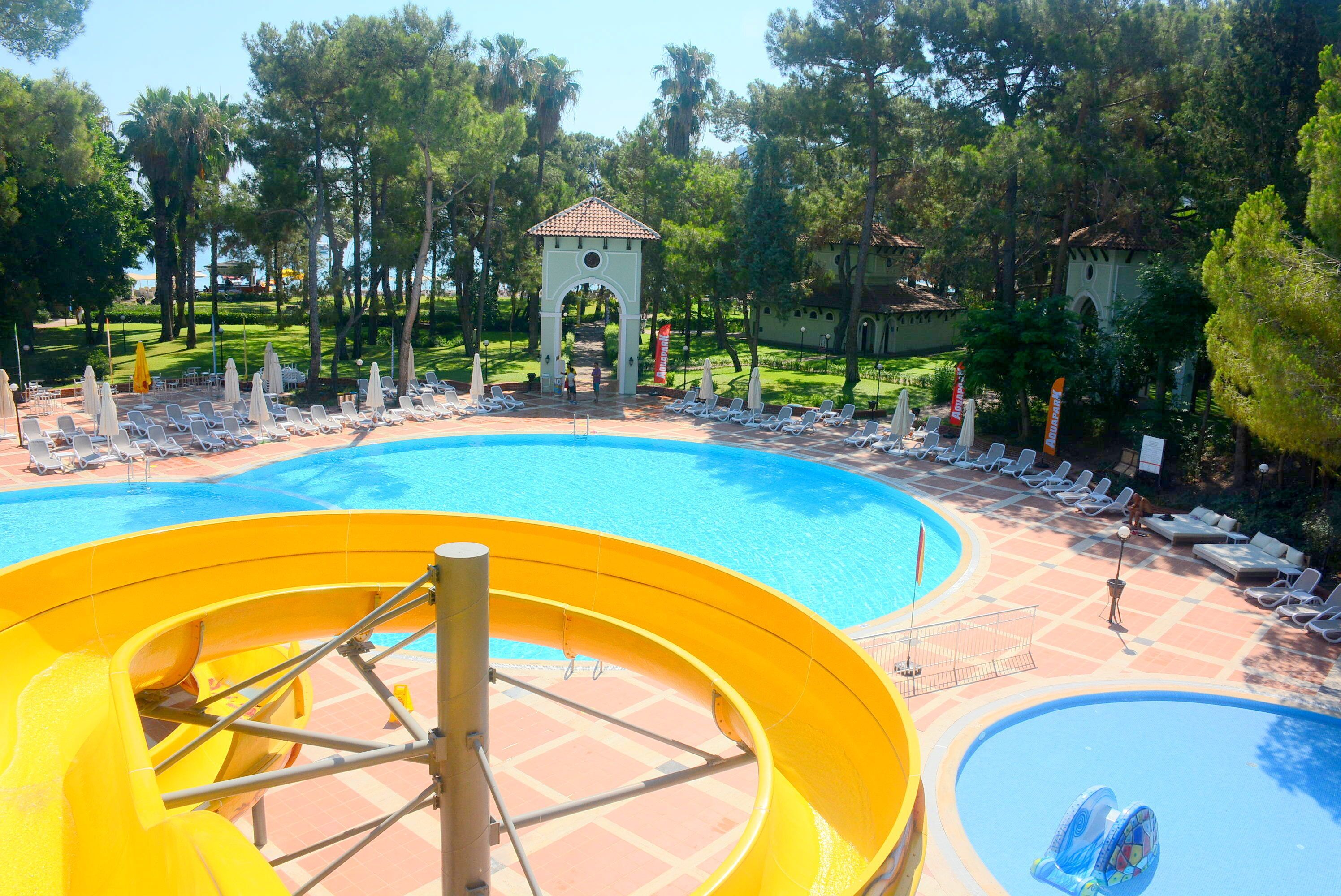 Un área de piscina con tobogán de agua, sillas de descanso y un pabellón.