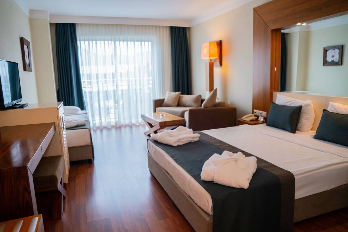 Une chambre d’hôtel équipée d’un lit, d’un bureau, d’une chaise, d’un canapé, d’une lampe et d’une fenêtre avec des rideaux.