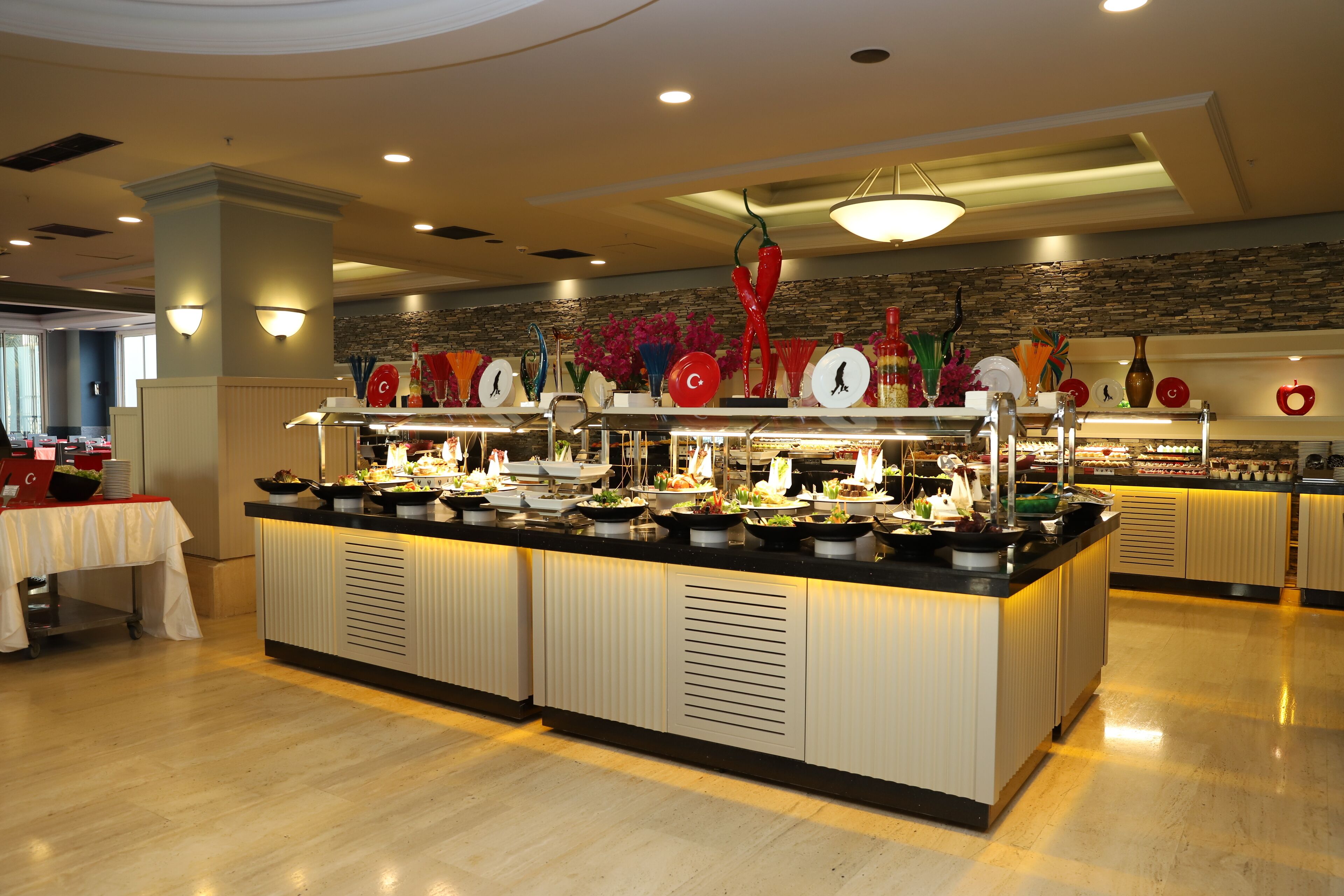 A buffet setup with multiple food stations, a white table with a red tablecloth, and a stone wall in the background.