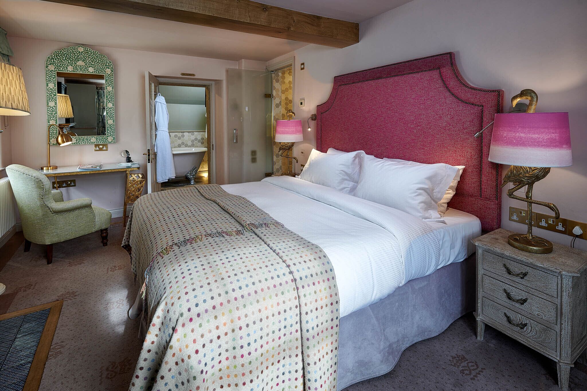 A bedroom with a large bed, a desk, a chair, and a vanity with a mirror.