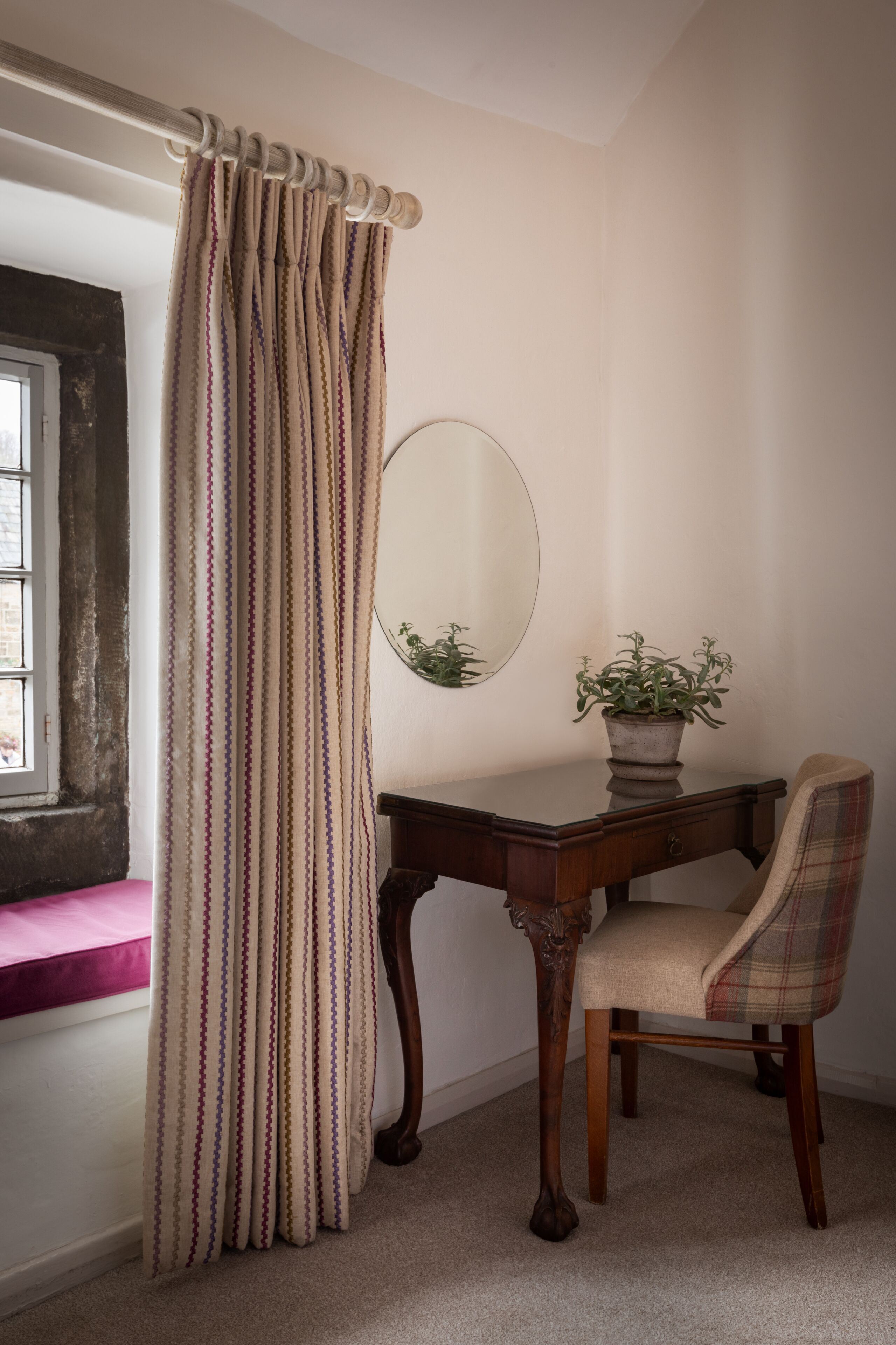 A room with a wooden desk, a chair, a potted plant, a mirror, and a striped curtain.