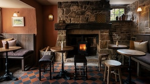 A cozy interior with a stone fireplace, wooden furniture, and a checkered floor pattern. - The Beeley Inn  (Matlock)