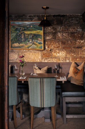 A dining area with a rustic stone wall, a painting, and a table set for two with chairs.