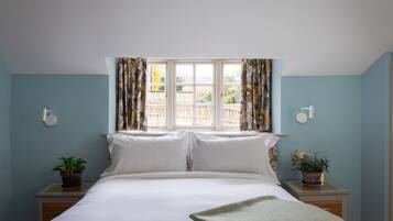 A bedroom with a bed, two bedside tables with potted plants, a window with curtains, and a wall-mounted light fixture.