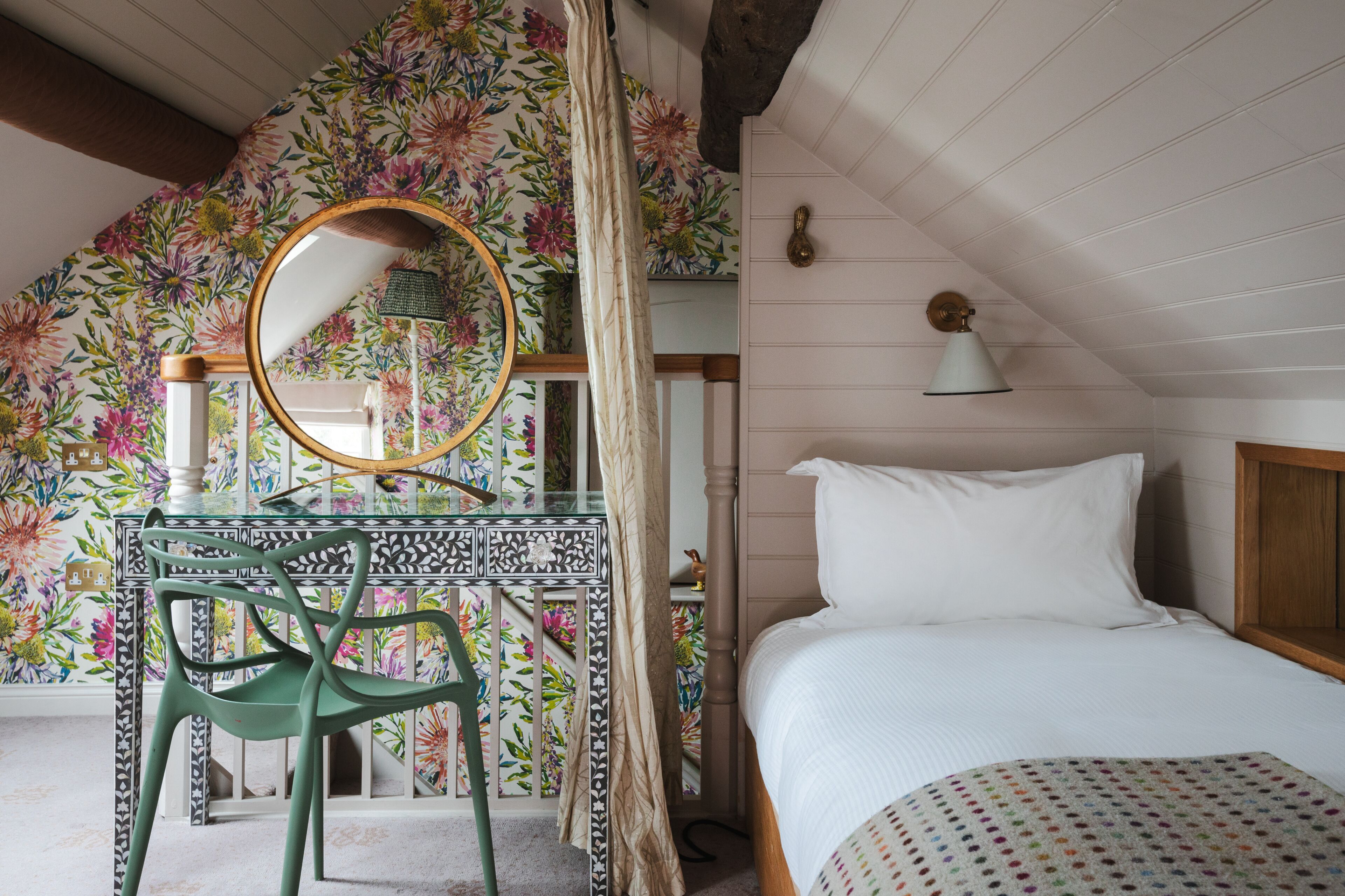 A bedroom with a bed, a desk with a chair, a mirror, and a lamp.