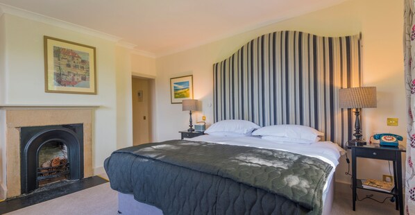 A hotel room with a bed, a fireplace, a striped curtain, and a nightstand with a lamp.