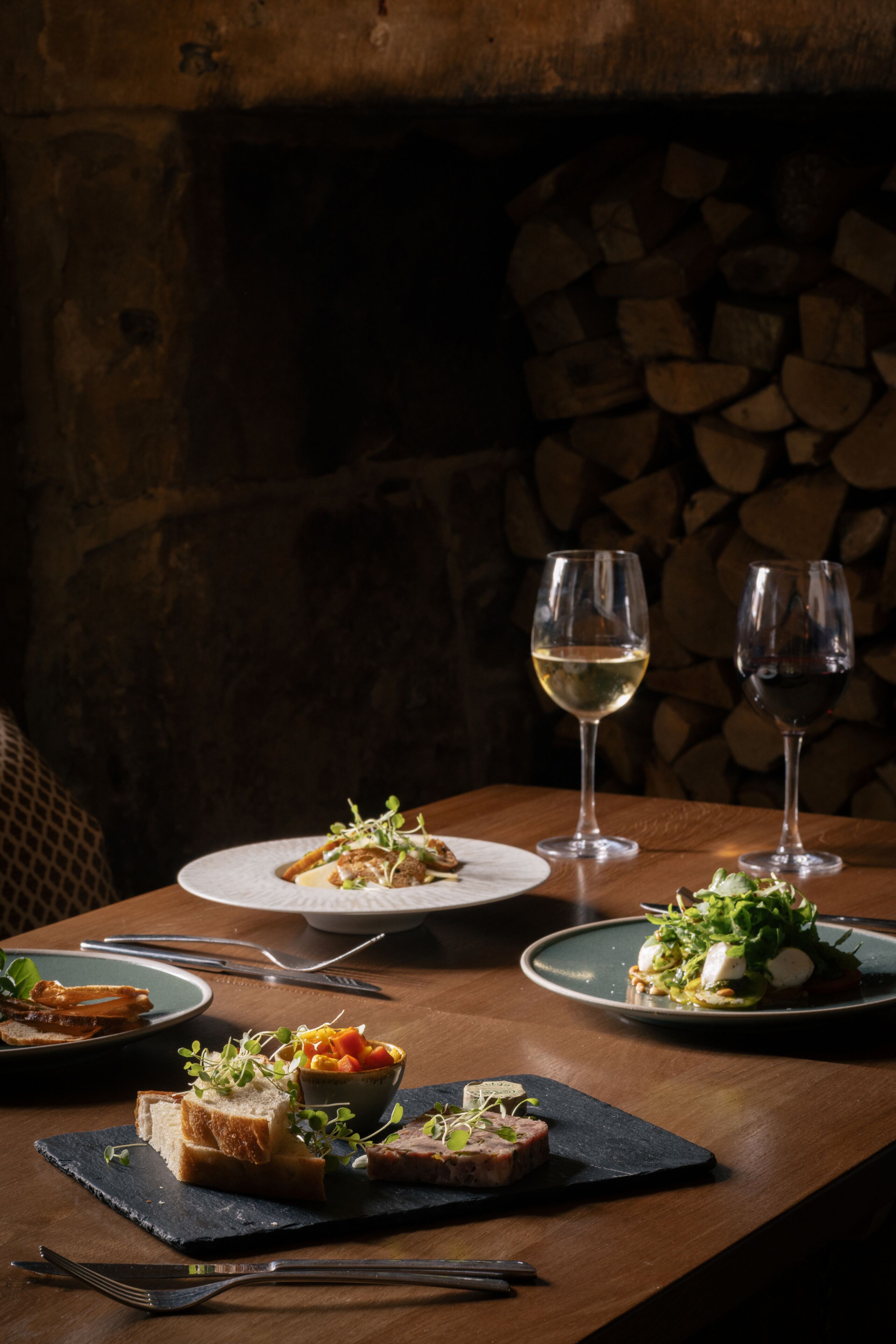 A dining table with plates of food, two wine glasses, and cutlery.