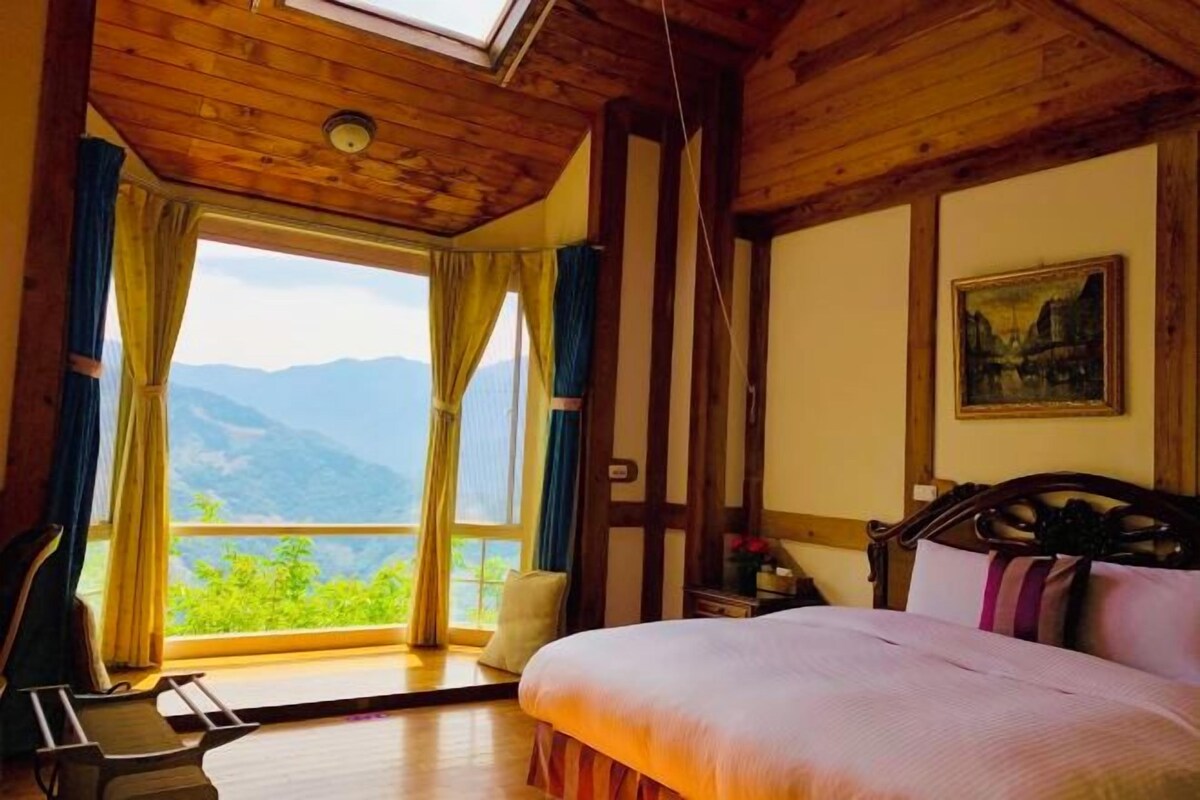A bedroom with a large window, a bed, and a painting on the wall.
