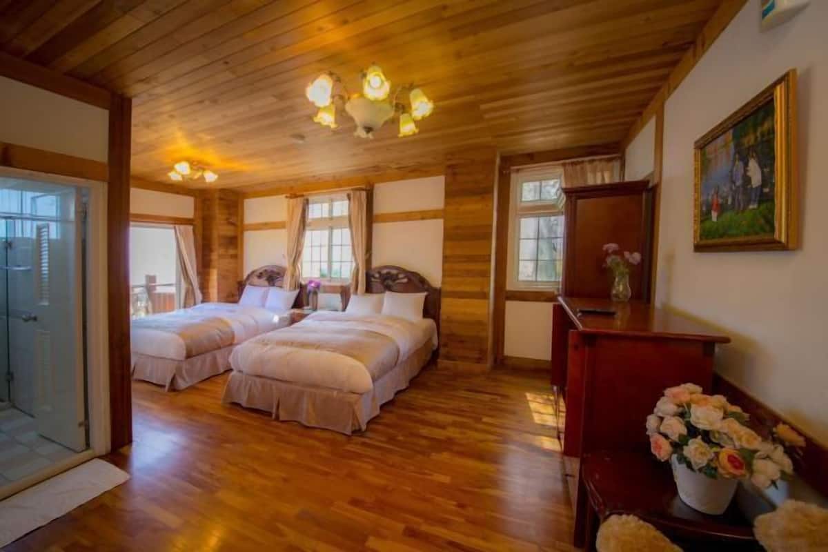 Ein Zimmer mit zwei Betten, Holzböden, einem Chandelier, einem Gemälde und einer Vase mit Blumen.
