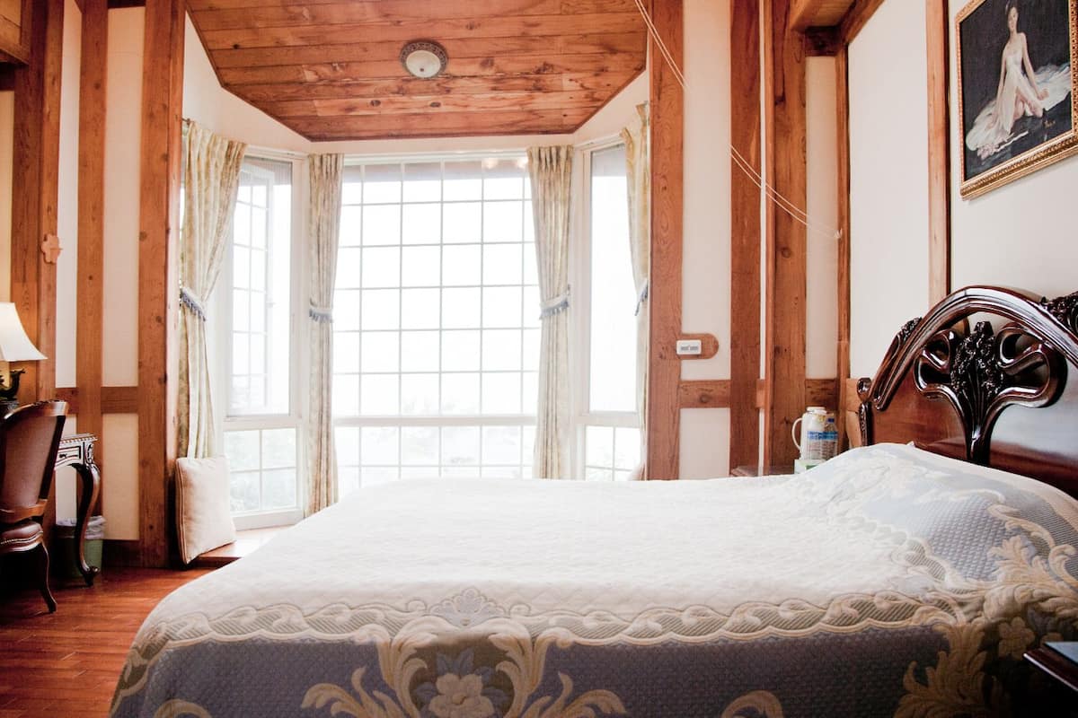 Ein Schlafzimmer mit Holzbalkendecke, einem großen Bett mit gemustertem Überwurf, einem Schreibtisch mit Lampe und einem Sessel.