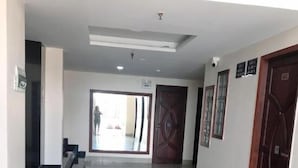 A hallway with a reflective floor, a large door with a geometric design, and a view into a room with a person visible through the door. - Hoa De Nhat Hotel (Ho Chi Minh City)