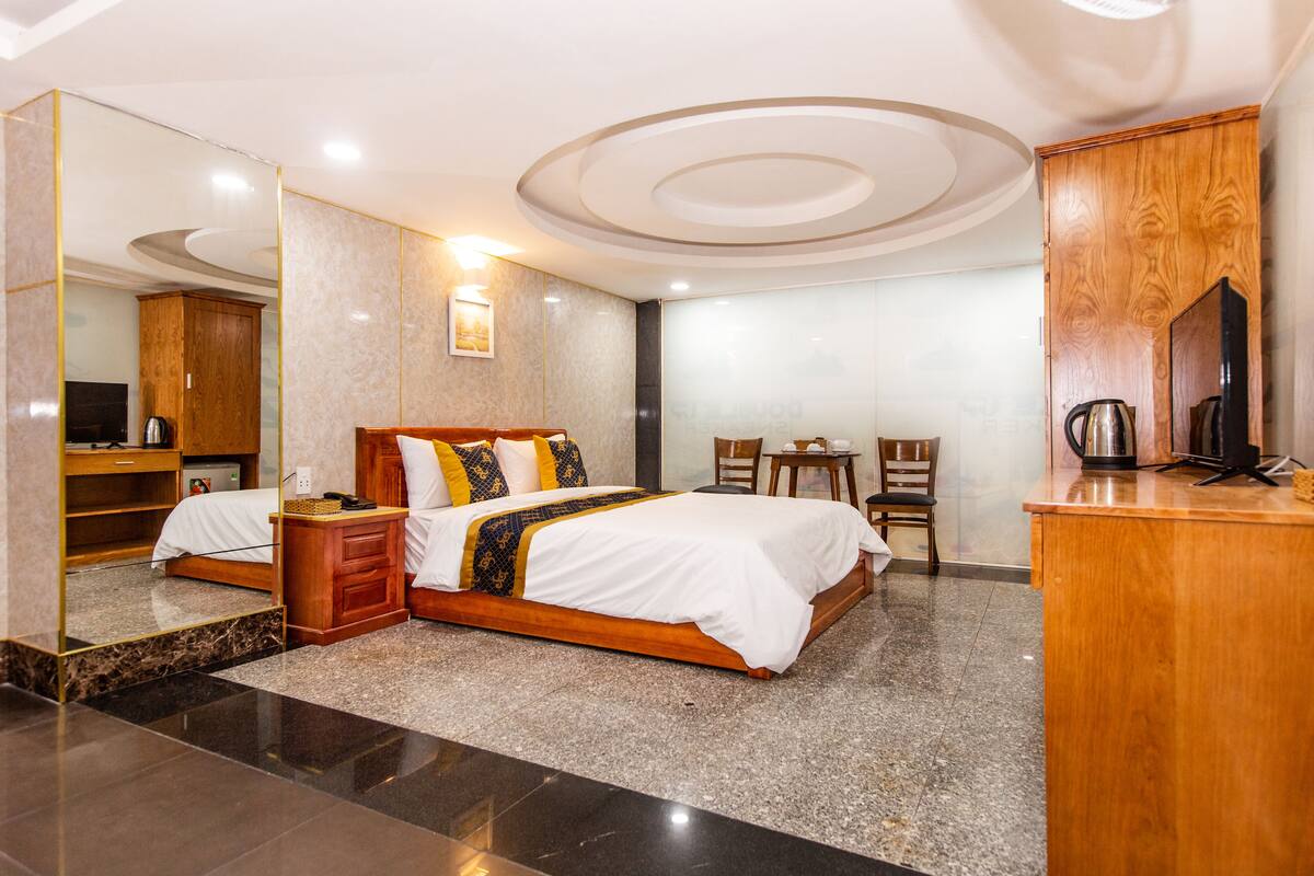Habitación de hotel con una cama grande, un escritorio de madera, una silla, una mesita y un espejo.