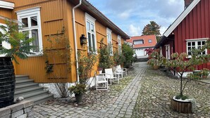 A cobblestone courtyard with wooden houses, a white outdoor seating area, and a small tree. - Toldgaarden Gjestegaard (Larvik)