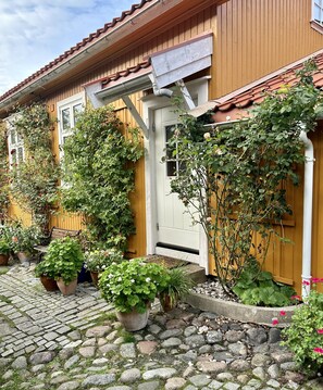 A wooden house with a tiled roof, a white door, and a stone-paved entrance. - Toldgaarden Gjestegaard (Larvik)
