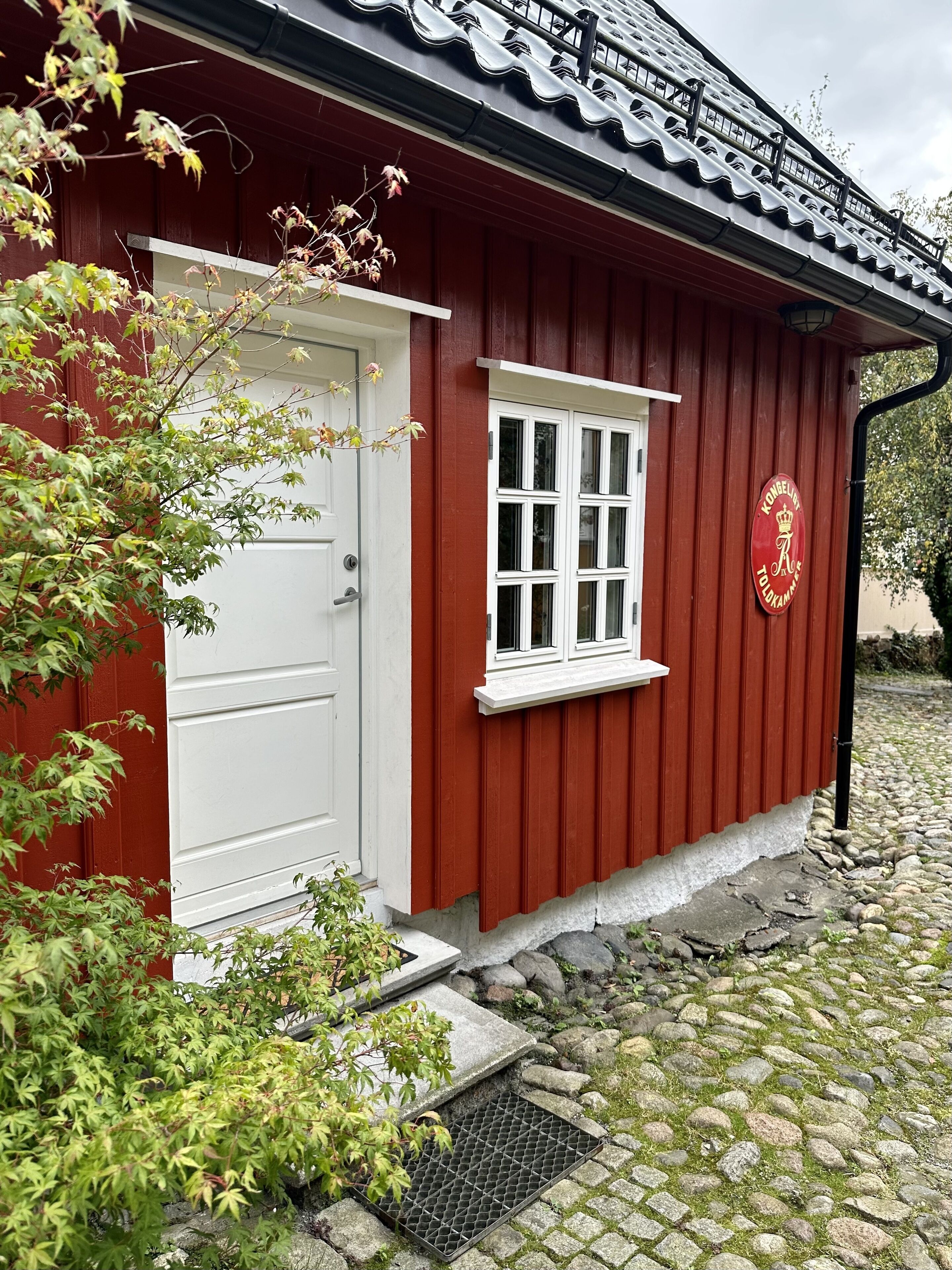 A red building with a white door and window, a stone pathway, and a metal grate.