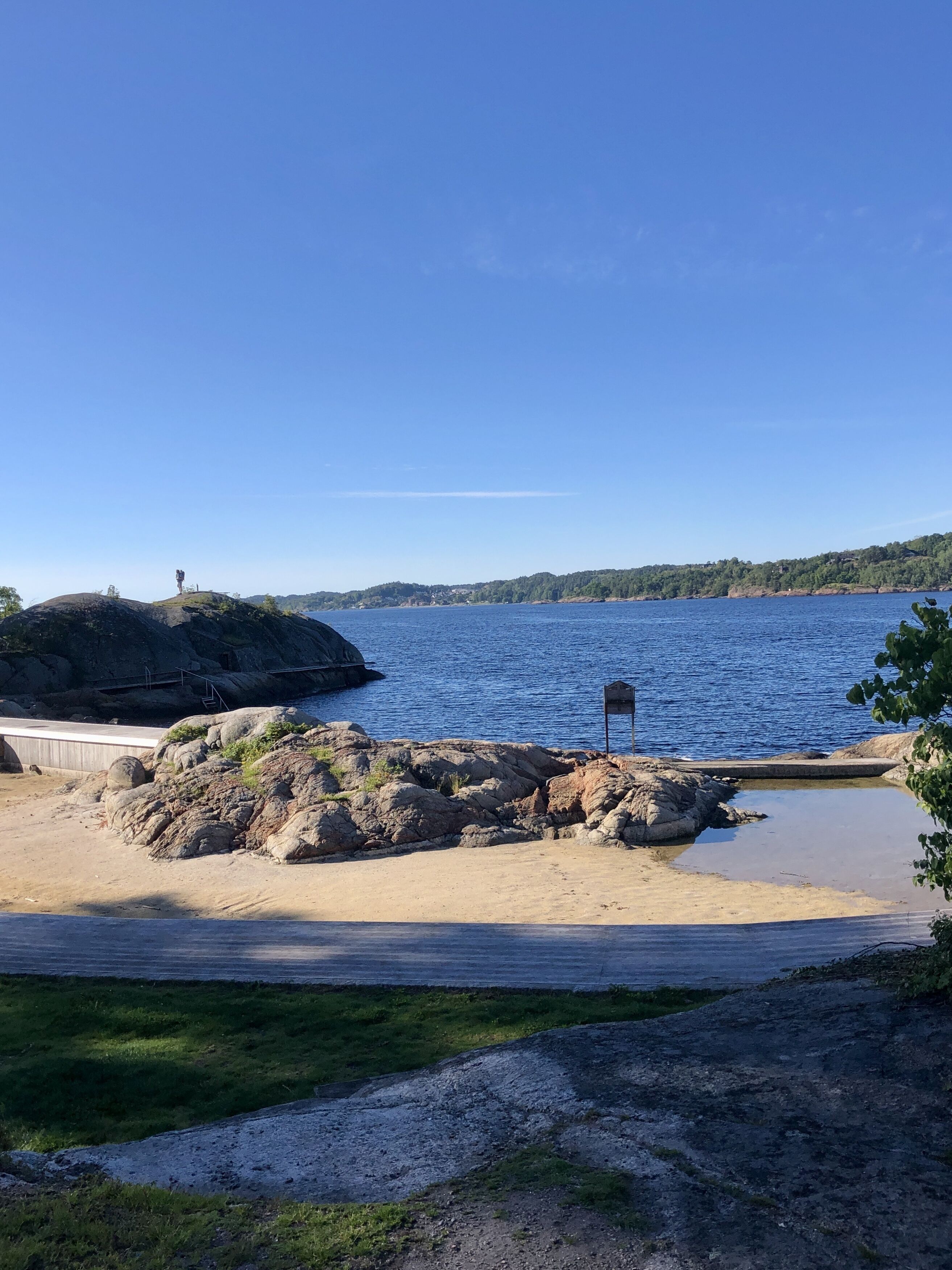 A coastal landscape with a rocky outcrop, a sandy beach, and a clear blue sky.