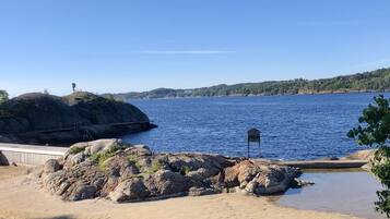 A coastal landscape with a rocky outcrop, a sandy beach, and a clear blue sky.