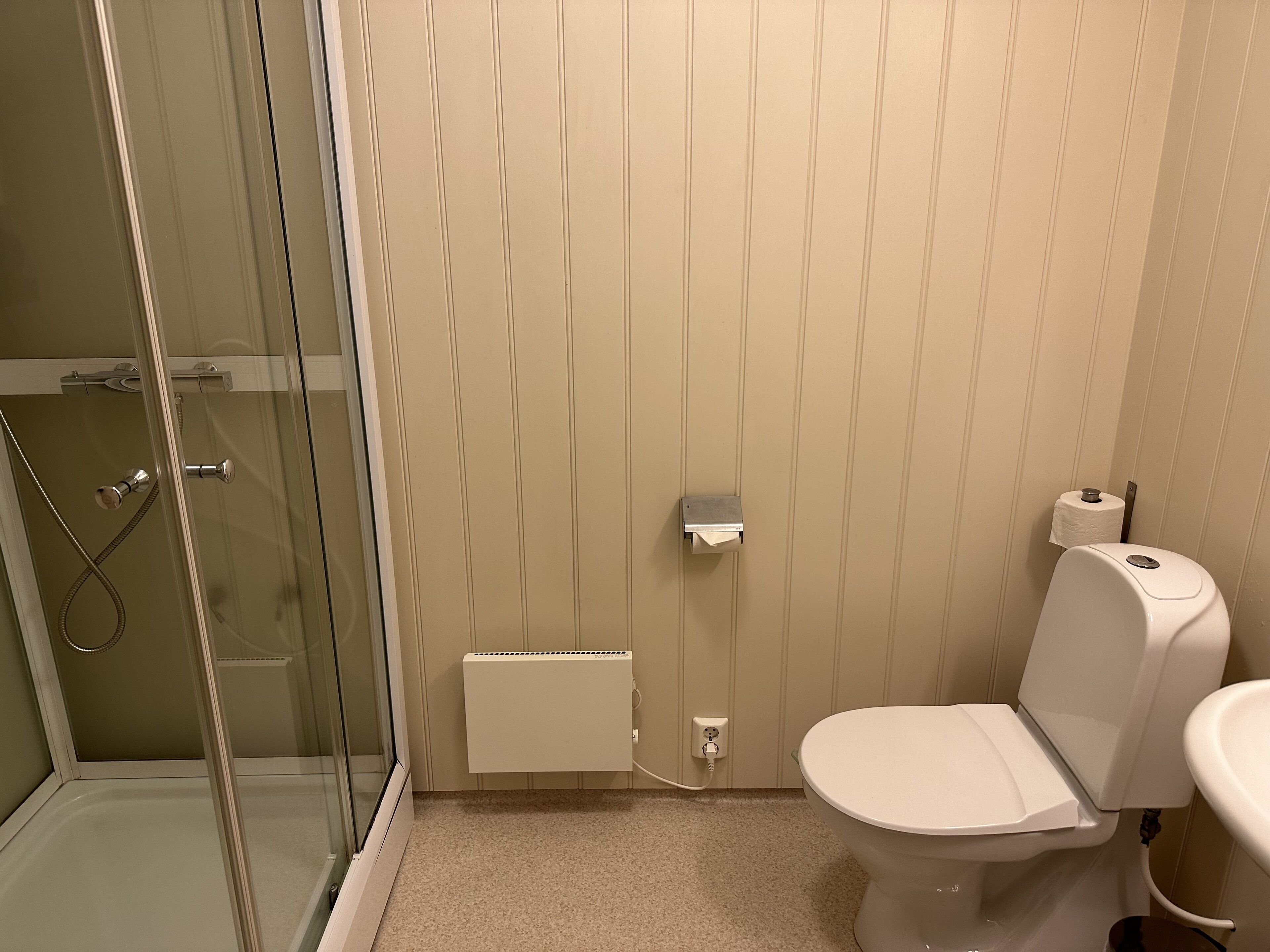 A bathroom with a glass shower enclosure, a toilet, and a sink.
