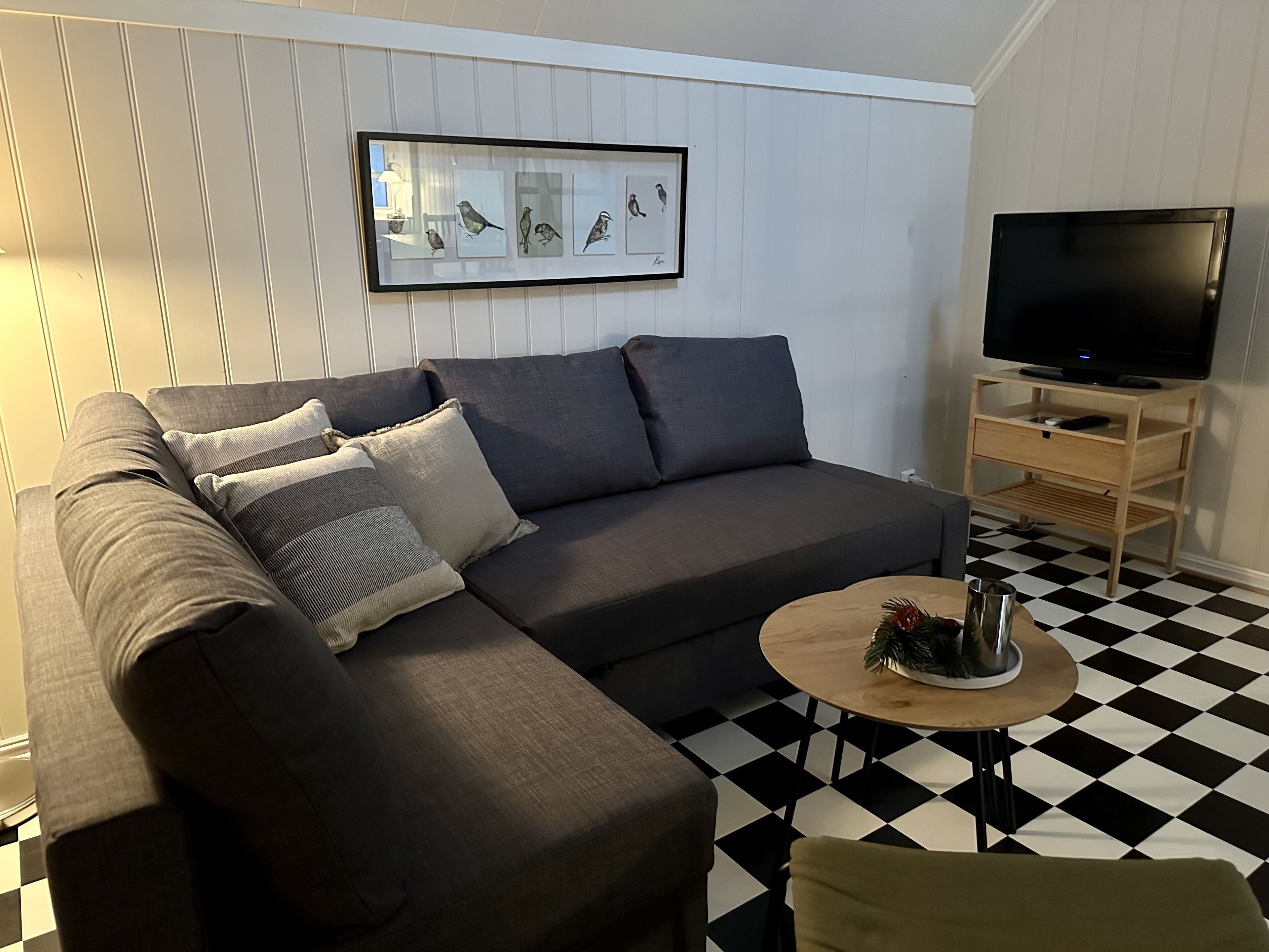 Una sala de estar moderna con un sofá modular, una mesa de centro, un televisor de pantalla plana sobre un atril de madera y un suelo a cuadros en blanco y negro.