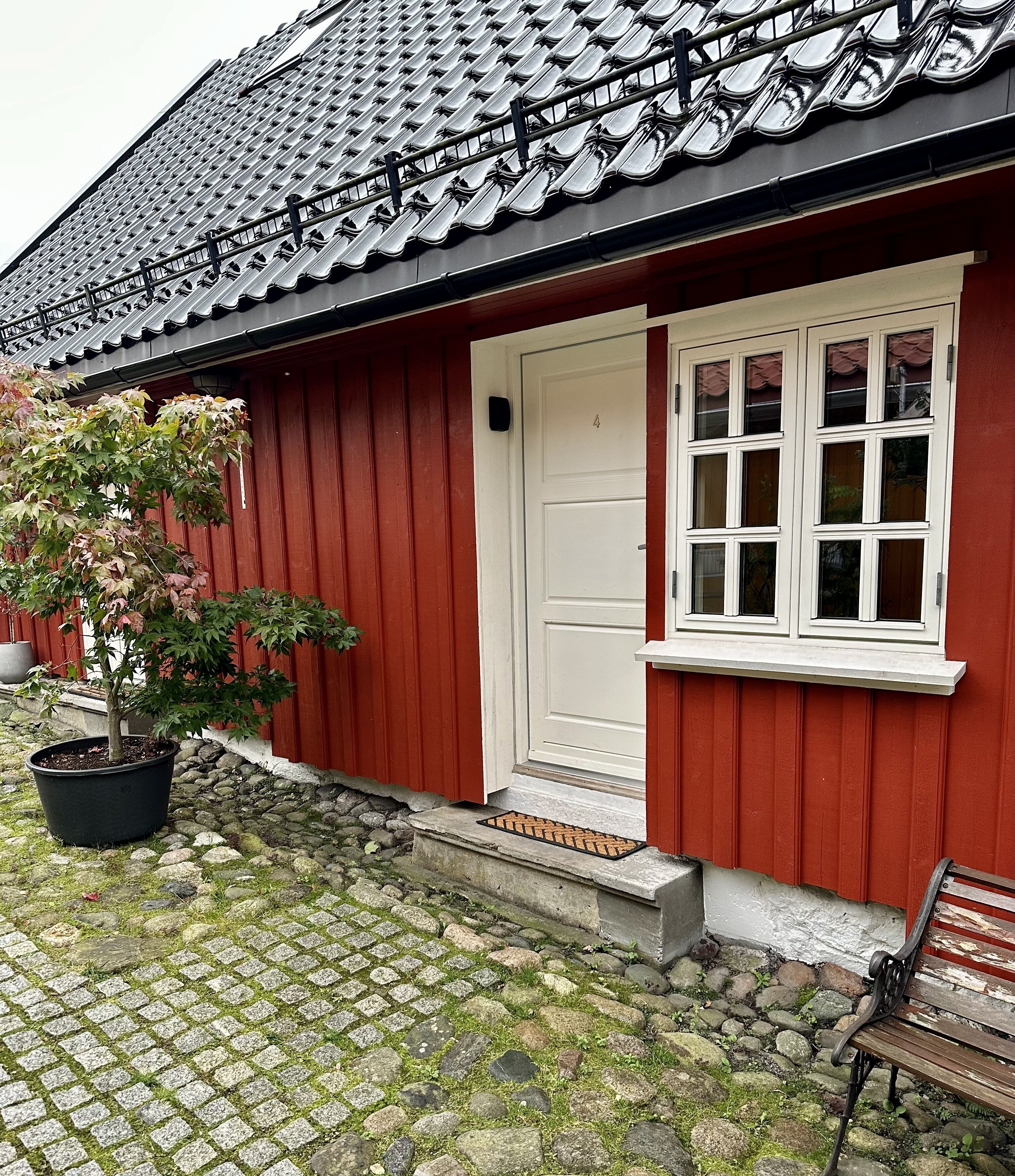 Un bâtiment rouge avec une porte et des fenêtres blanches, un arbre en pot et un banc.