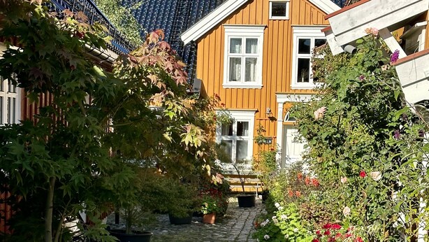 A cobblestone pathway leading to a wooden house with a sloped roof and multiple chimneys. - Toldgaarden Gjestegaard (Larvik)
