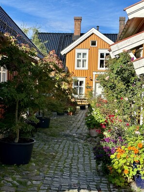 A cobblestone pathway leading to a wooden house with a sloped roof and multiple chimneys. - Toldgaarden Gjestegaard (Larvik)