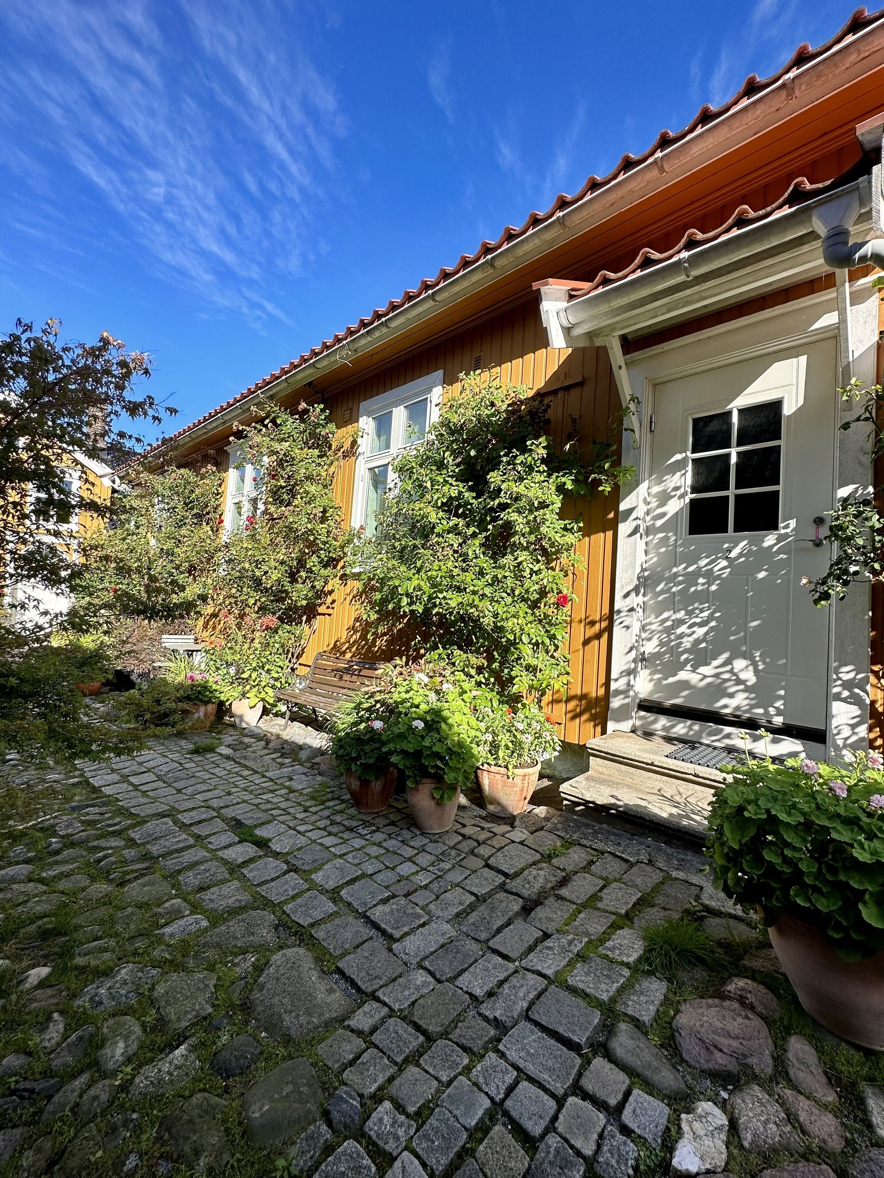 A traditional wooden house with a tiled roof, a white door, and potted plants in the garden area.