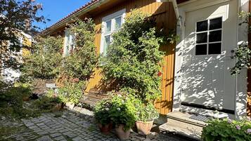 A traditional wooden house with a tiled roof, a white door, and potted plants in the garden area.