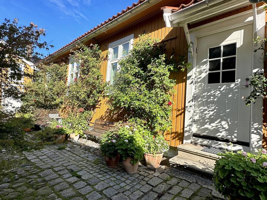 A traditional wooden house with a tiled roof, a white door, and potted plants in the garden area.