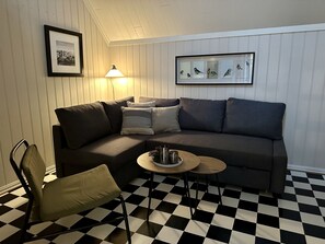 A living room with a checkered floor, a sofa, a lamp, a framed picture, and a small table. - Toldgaarden Gjestegaard (Larvik)