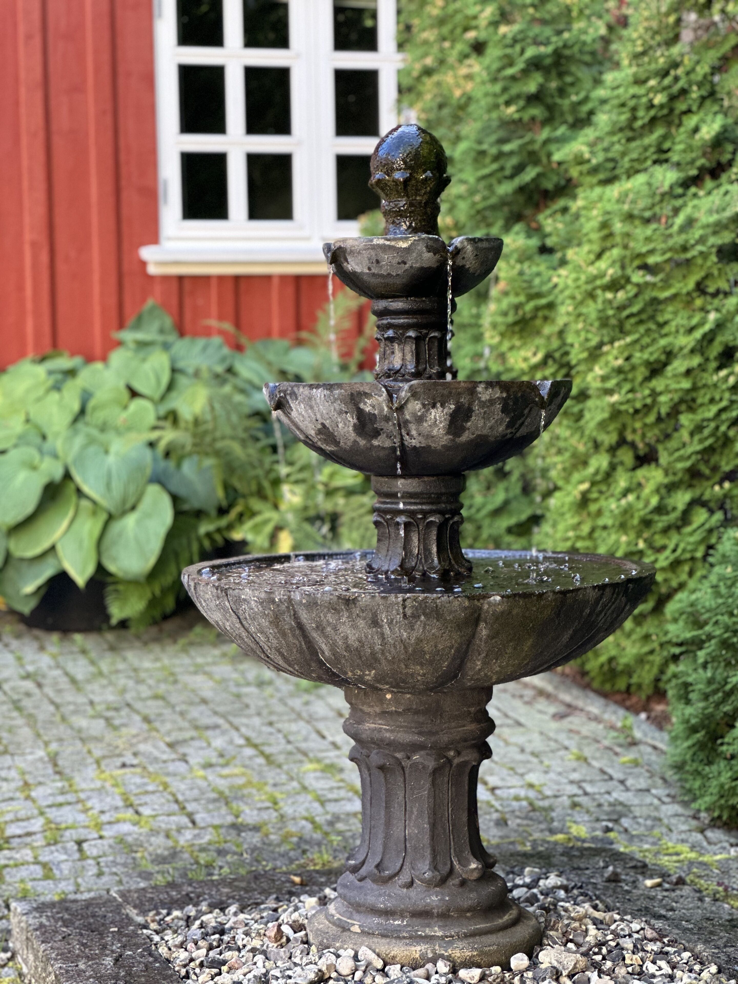 A stone fountain with a tiered design, set on a stone surface with pebbles.