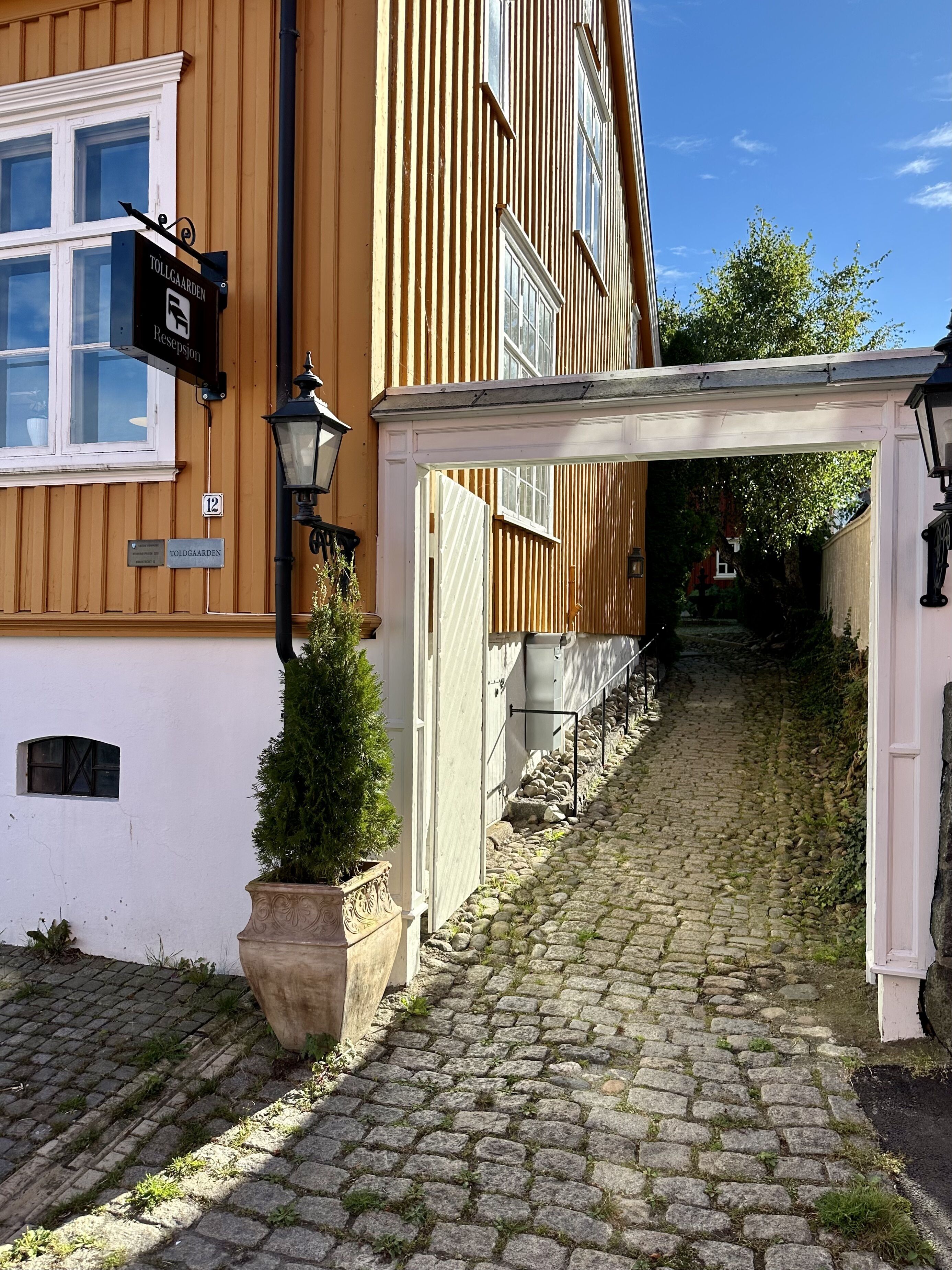 A cobblestone alley leading to a building with a wooden facade and a sign reading "TOLLAGAARDEN."