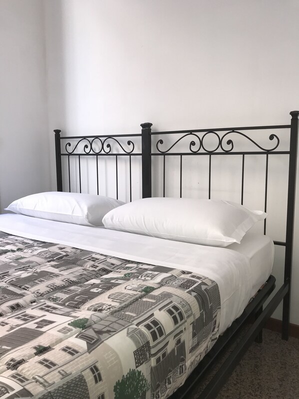 A bed with a metal headboard, white bedding, and a patterned bedspread. - Elite Loreto Milano (Milan)