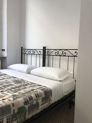 A bed with a metal frame, white bedding, and a patterned bedspread. - Elite Loreto Milano (Milan)