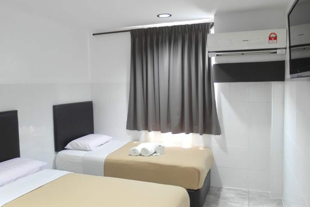 A hotel room with two beds, a flat-screen TV, an air conditioning unit, and a window with curtains.