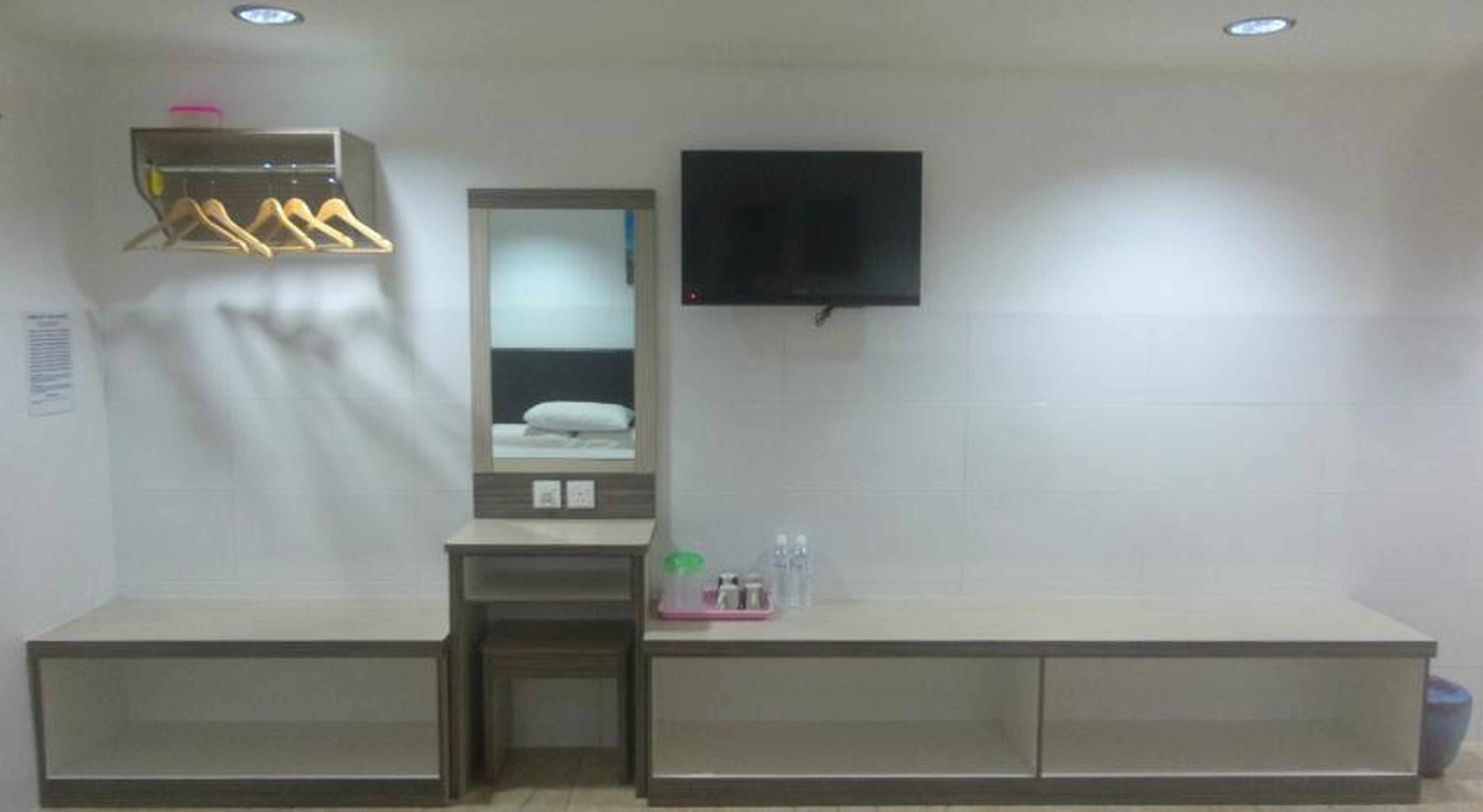 Une salle de bain d’hôtel avec un miroir, un téléviseur fixé au mur et une étagère contenant des articles de toilette.
